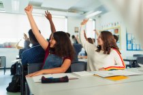 High school girl students with hands raised during lesson in classroom — Stock Photo