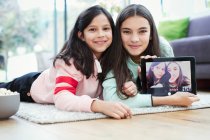 Portrait smiling sisters using digital tablet camera on living room floor — Stock Photo