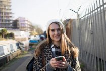 Portrait smiling young woman with smart phone on urban sidewalk — Stock Photo