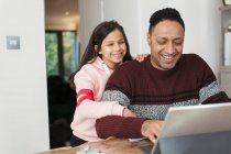 Усміхнений батько і дочка використовують цифровий планшет за столом — стокове фото