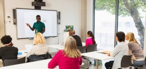 Community college students watching instructor leading lesson at projection screen in classroom — Stock Photo