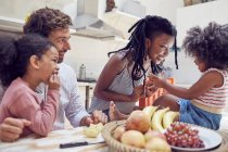 Молодая семья ест фрукты на столе — стоковое фото