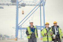 Dock workers and manager walking below crane at shipyard — Stock Photo