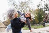 Портрет игривой бабушки, поднимающей внучку на детской площадке — стоковое фото