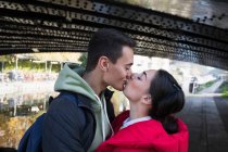 Liebevolles junges Paar küsst sich unter Brücke — Stockfoto