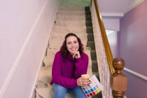 Portrait confident woman redecorating, holding paint swatch on stairs — Stock Photo