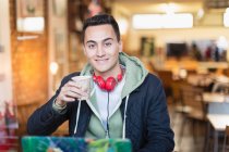 Ritratto sorridente, fiducioso giovane studente di college maschile che studia e beve caffè nella finestra del caffè — Foto stock