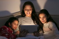 Мать и дочери используют цифровые планшеты в темной спальне — стоковое фото