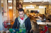 Сосредоточенный молодой студент колледжа учится за ноутбуком в витрине кафе — стоковое фото