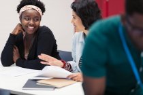 Smiling female community college students discussing paperwork in classroom — Stock Photo