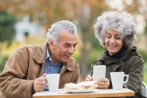 Couple aîné avec téléphone intelligent, déjeuner et boire du café dans le parc — Photo de stock