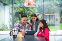 Padre e hijas usando tableta digital en la mesa del desayuno - foto de stock