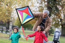 Grandfather and grandchildren flying a kite in autumn park — Stock Photo