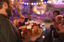 Человек, подающий поднос пива друзьям на вечеринке в саду — стоковое фото