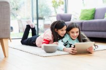 Chicas viendo películas con tabletas digitales en el piso de la sala de estar - foto de stock