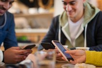 Young adult friends using smart phones at cafe table — Stock Photo