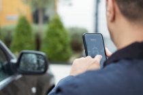 Человек устанавливает автомобильную сигнализацию со смартфона на подъездной дорожке — стоковое фото