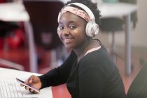 Portrait smiling, confident female college student with smart phone and headphones in classroom — Stock Photo