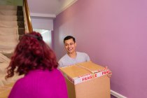 Happy couple moving into new house, carrying cardboard boxes up stairs — Stock Photo