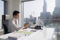 Empresário usando telefone inteligente em ensolarado, escritório urbano — Fotografia de Stock