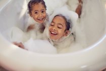 Retrato juguetonas hermanas disfrutando de baño de burbujas - foto de stock