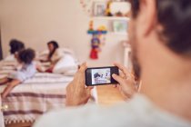 Padre con fotocamera telefono fotografare la famiglia sul letto — Foto stock