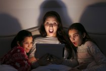 Surprised mother and daughters watching movie on digital tablet in dark bedroom — Stock Photo