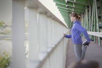 Joven corredora estirando pierna en barandilla urbana - foto de stock