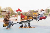 Grandfather and granddaughter playing on seesaw at playground — Stock Photo