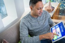 Hombre configurar la alarma del hogar inteligente de la tableta digital en el sofá de la sala de estar - foto de stock