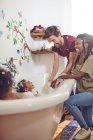 Padres juguetones dando a las hijas baño de burbujas - foto de stock