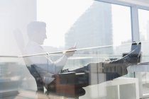 Businessman using smart phone in sunny, urban office — Stock Photo