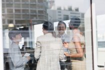 Des hommes d'affaires souriants parlent à la fenêtre ensoleillée du bureau — Photo de stock