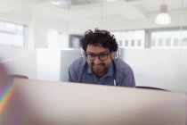 Hombre de negocios sonriente con auriculares trabajando en la computadora en la oficina - foto de stock