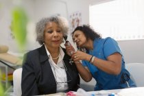Женщина-врач осматривает ухо пожилого пациента с помощью отоскопа в кабинете врача — стоковое фото