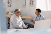 Médico varón hablando con el paciente en el consultorio médico - foto de stock