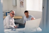 Reunião de médico masculino com paciente sênior em computador em consultório médico — Fotografia de Stock