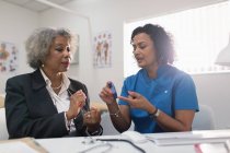 Женщина-врач учит пациента диабету, как использовать глюкометр в офисе врача — стоковое фото