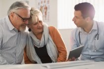 Male doctor with digital tablet meeting with senior couple in doctors office — Stock Photo