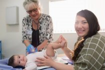 Portrait happy mother with baby daughter and pediatrician in examination room — Stock Photo