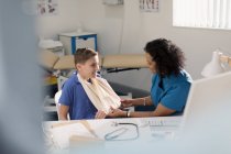 Female doctor checking arm sling of boy patient in doctors office — Stock Photo