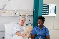 Paziente femminile che mostra fiori all'infermiera nella stanza d'ospedale — Foto stock