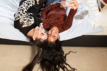Happy teenage girls taking selfie with smart phone on bed — Stock Photo