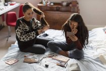 Teenage girls applying makeup and brushing hair on bed — Stock Photo