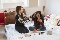 Teenage girls applying makeup and brushing hair on bed — Stock Photo