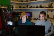 Happy teenage boys with headsets playing video games at computer in dark room — Stock Photo