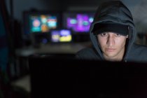 Männlicher Hacker im Kapuzenpulli benutzt Computer im dunklen Raum — Stockfoto