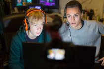 Teenage boys with headphones playing video game at computer in dark room — Stock Photo