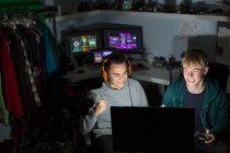 Excited teenage boys with headphones playing video game at computer in dark room — Stock Photo