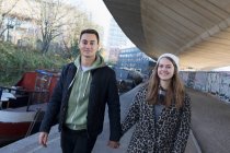 Portrait happy young couple holding hands, walking along urban canal — Stock Photo